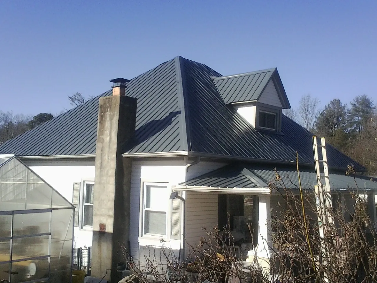 Dark blue standing seam metal roof on a white farmhouse with dormer — Slate & Tile Roof Repair by Roofing Brothers in Hague