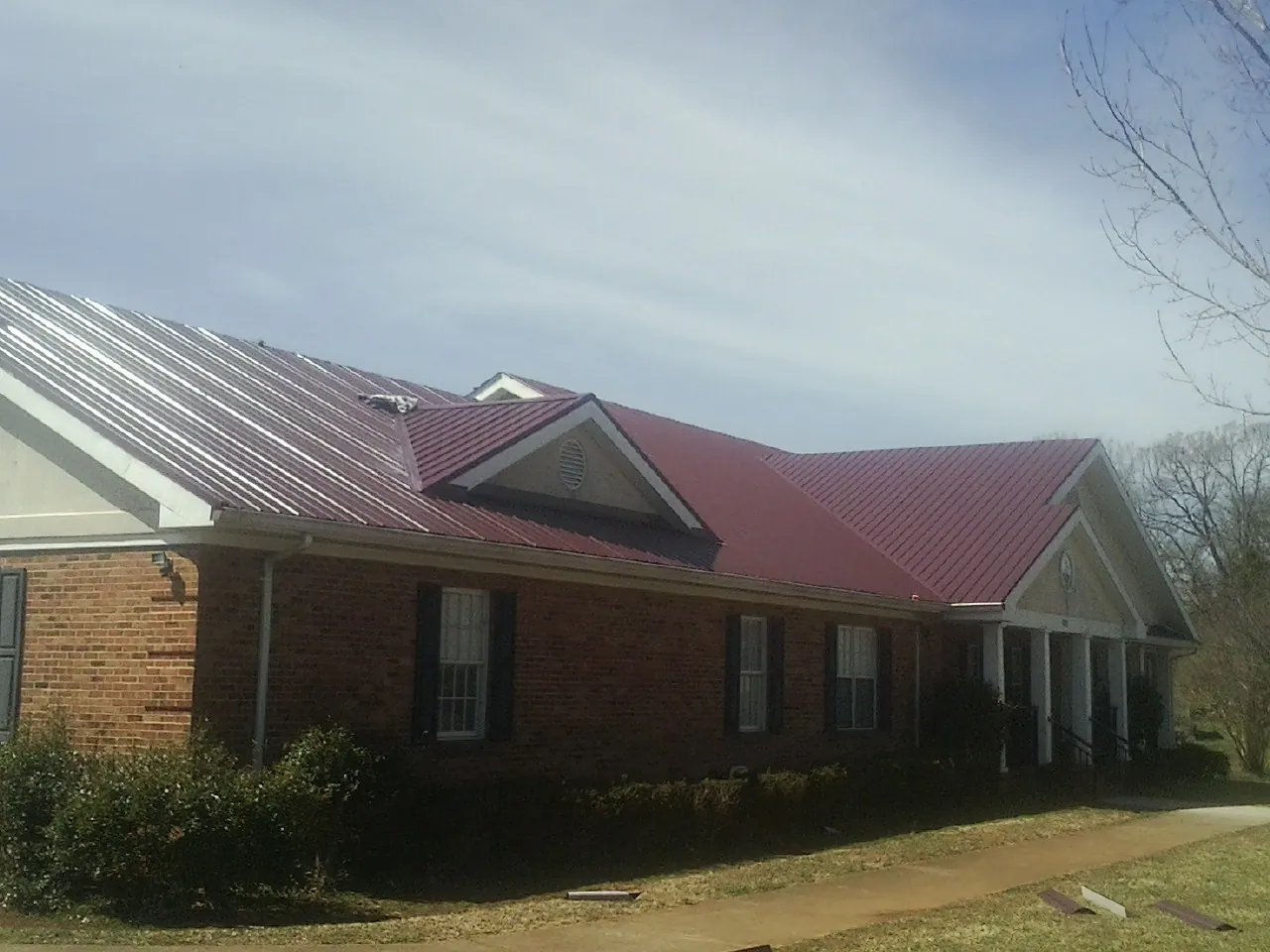 Red metal roof with gabled entries on a long brick building, from a Hail Damage Roof Repair job in Hague