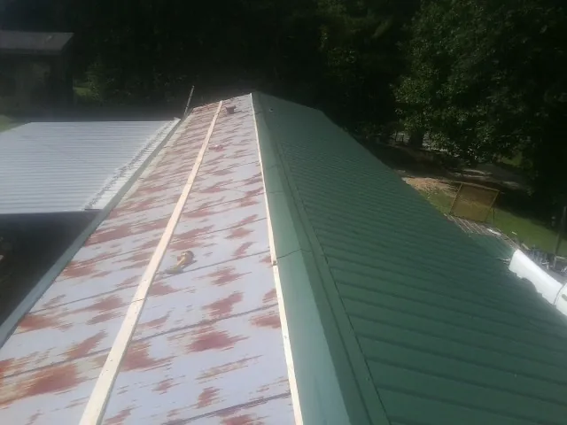 Old rusted panels beside newly installed green metal roofing — Wind Damage Roof Repair by Roofing Brothers in Hague