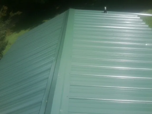 New green metal panels meeting at the ridge of a roof — Flat Roof Repair work by our crew in Hague