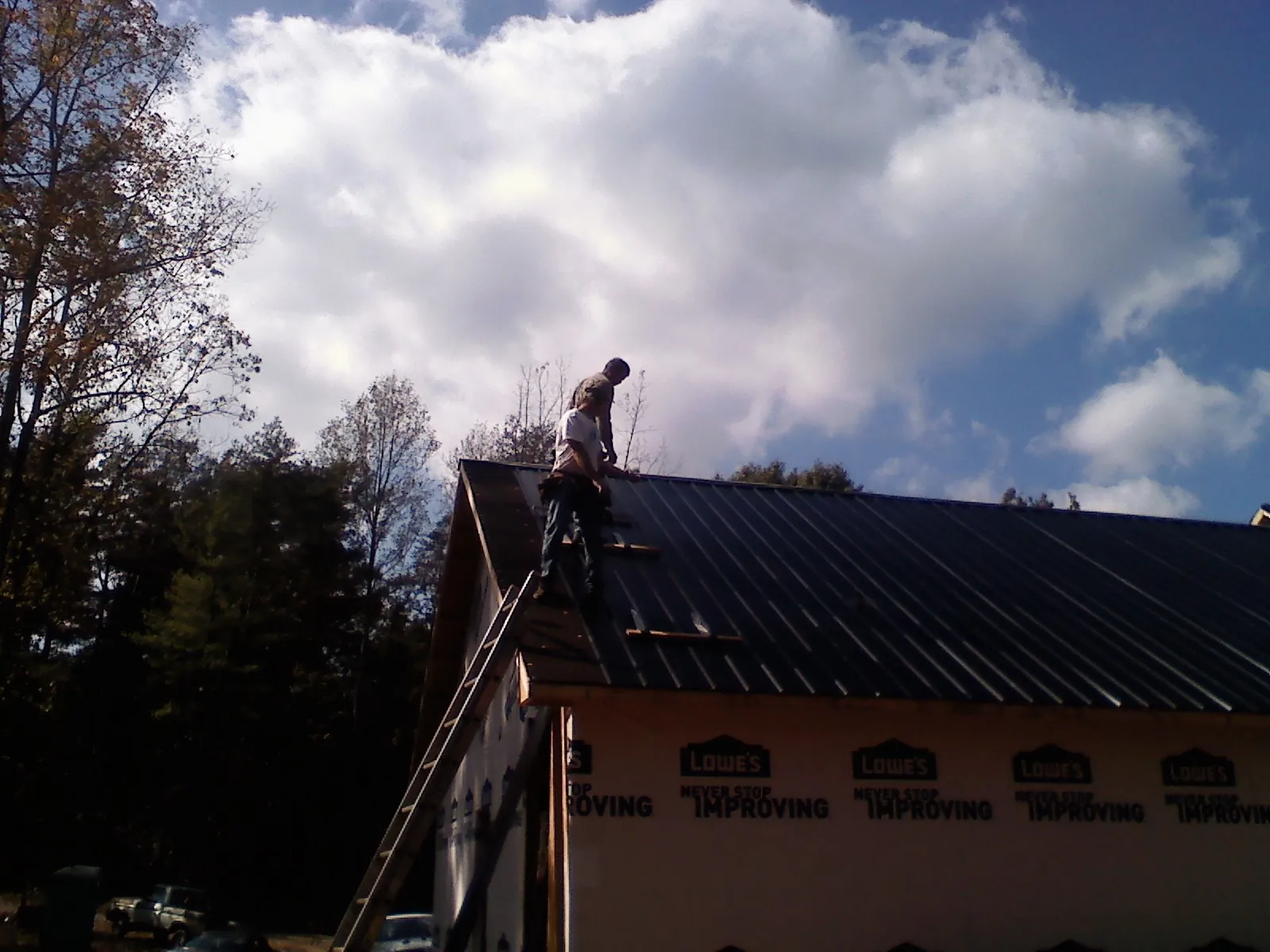 Roofer fastening dark metal panels high against a cloudy sky, from a Roof Inspection job in Hague