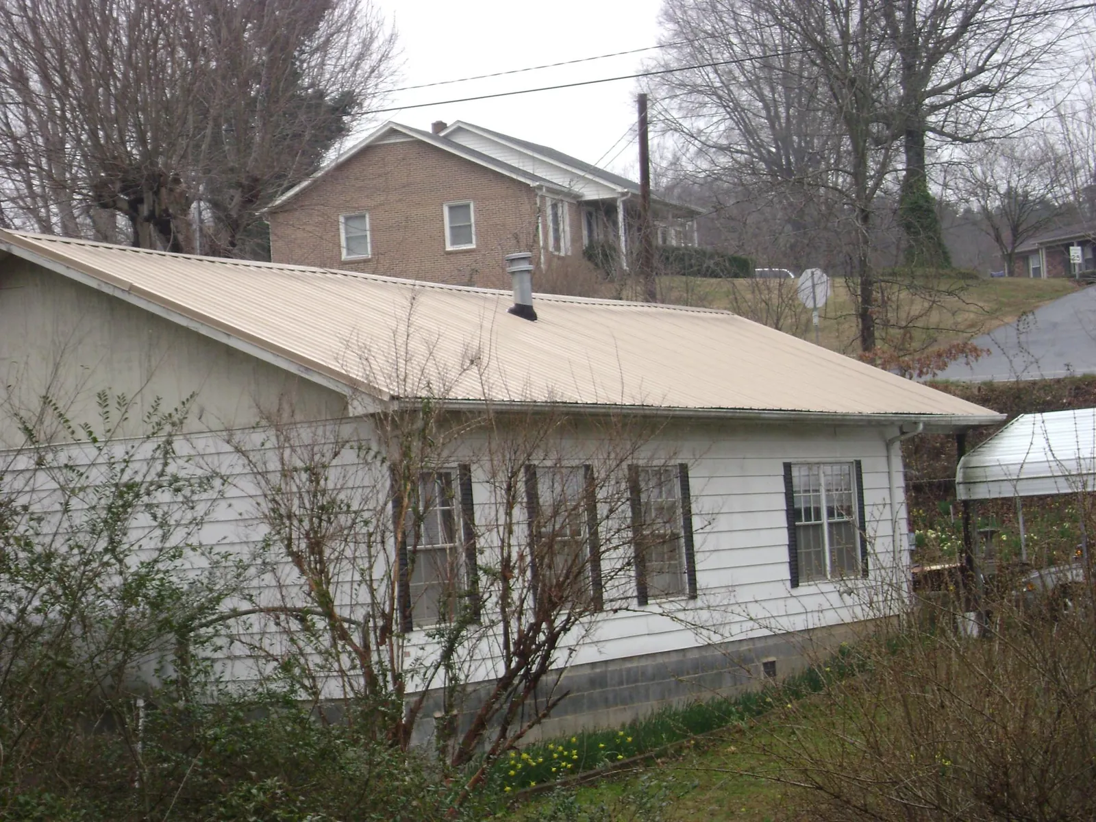 Tan metal roof on a white sided house set into a hillside — Commercial Roofing by Roofing Brothers in Hague