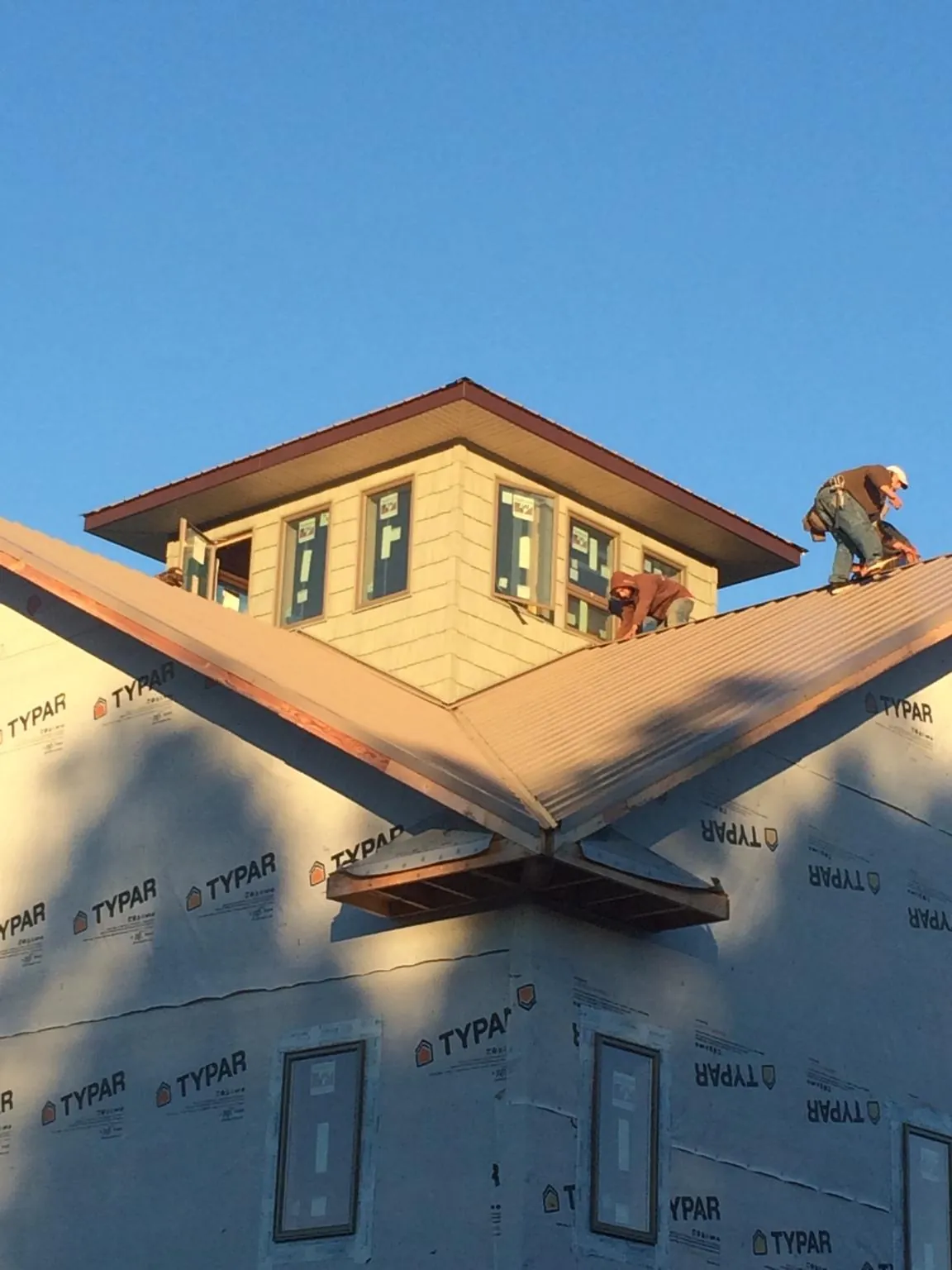 Roofers working around a rooftop cupola on a new metal roof at sunset — Roof Waterproofing in Hague by Roofing Brothers